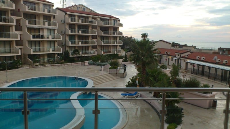 View from the balcony of the pool and residential complex in Pržno, Montenegro: modern architecture, palm trees, and a sea view.