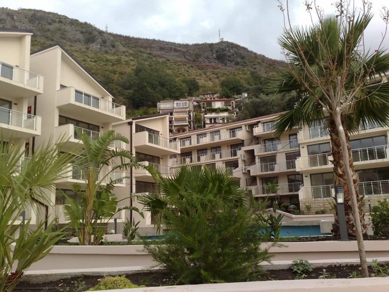 Modern residential complex with a pool and palm trees in Pržno, Montenegro: view of the apartment facades and mountains.