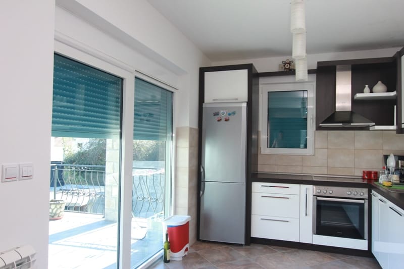 Modern kitchen in a house in Stoliv, Montenegro: light cabinetry, built-in appliances, and access to the terrace.