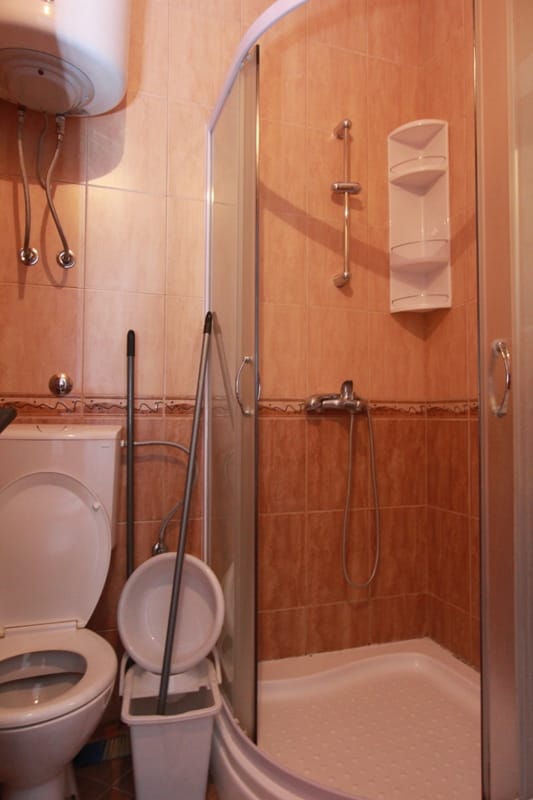 Bathroom with a shower cabin and boiler in a house in Stoliv, Montenegro. Light tiles, plumbing fixtures, interior.