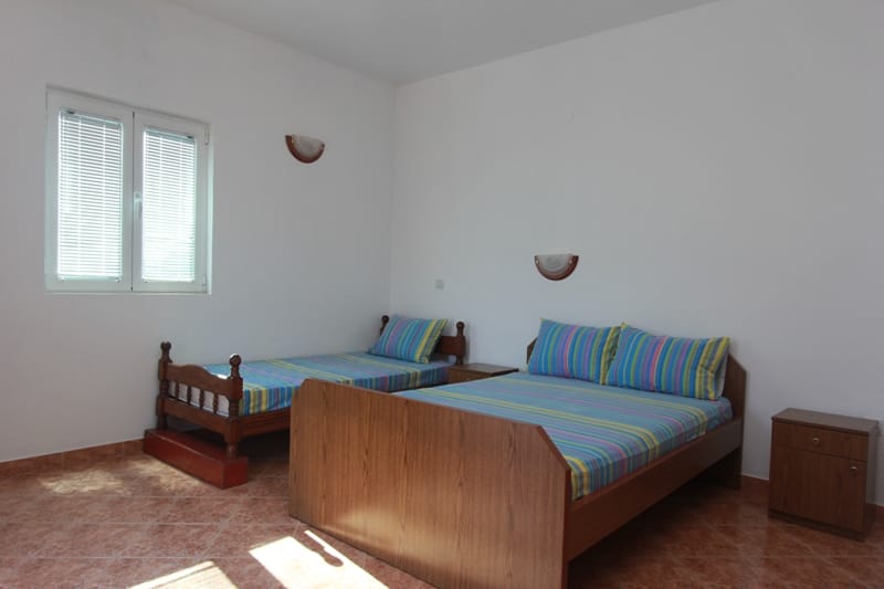 Bright bedroom with wooden beds in a house for sale in Stoliv, Montenegro: tiled floor and a view from the window.