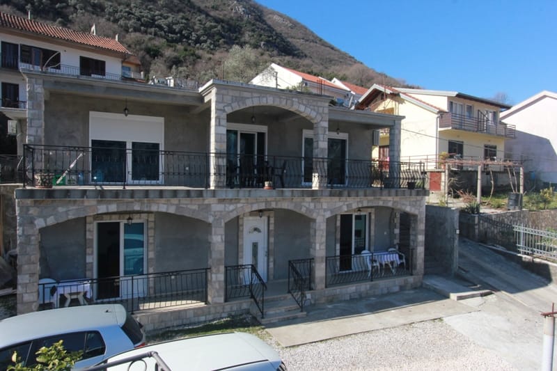 Two-story house with stone cladding and terraces in Stoliv, Montenegro: front view and on-site parking.