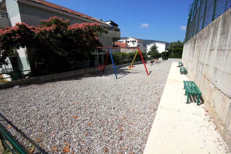 Children's playground with swings and benches near a residential building in Đenovići, Montenegro, view of the courtyard area.