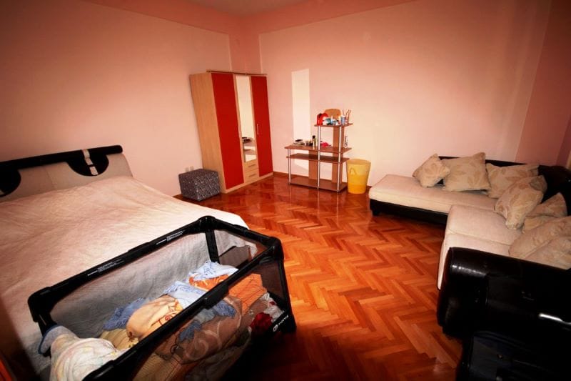 Bedroom in a house in Đenovići, Montenegro: double bed, baby playpen, corner sofa, and wardrobe on a parquet floor.