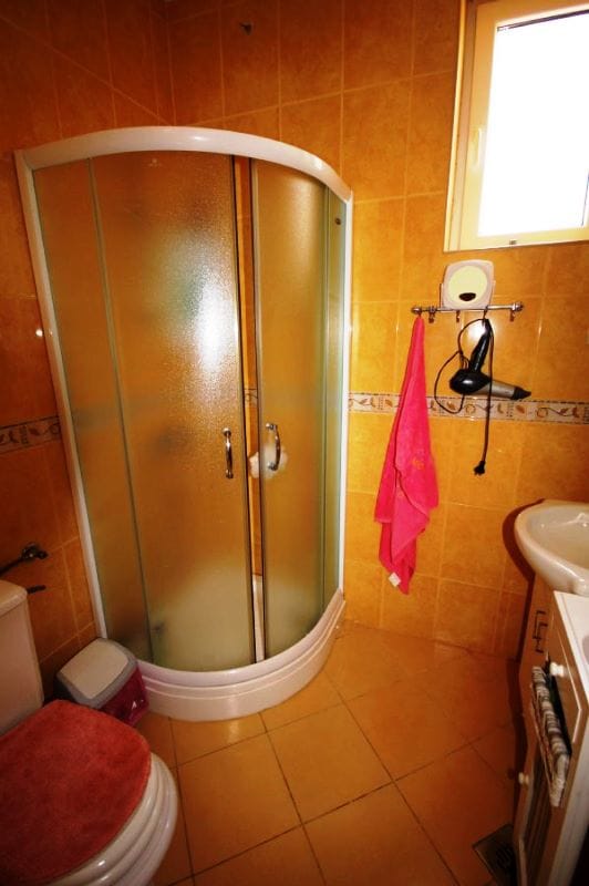 Bathroom with shower cabin in a house, Đenovići, Montenegro: warm-toned tiles, plumbing fixtures, and a window.