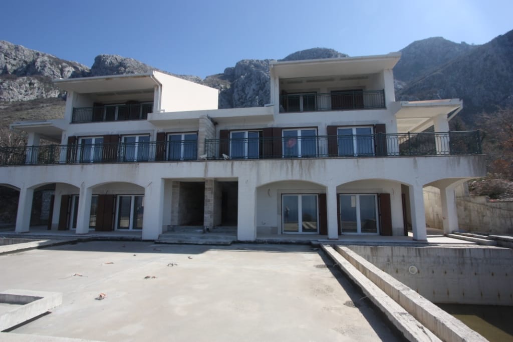 Two-story villa in Blizikuće, Montenegro: facade with terraces, panoramic windows, and mountain views by the pool.