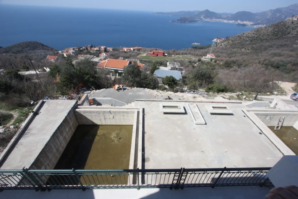 An open-air swimming pool under construction at a villa in Blizikuće, Montenegro, with panoramic views of the Adriatic Sea and the mountains.