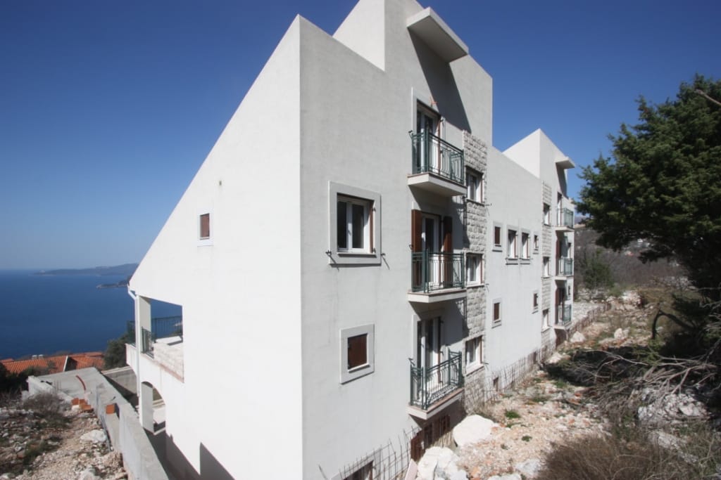 Modern villa in Blizikuće, Montenegro: facade with balconies, stone cladding, and panoramic views of the Adriatic Sea.