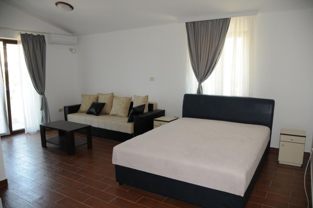 Bright bedroom with a double bed and sofa in a villa in Markovichi, Montenegro: tiled floor, panoramic windows.