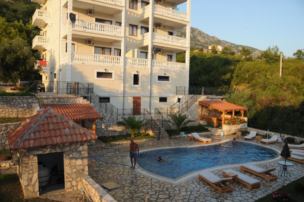 Villa in Markovichi, Montenegro: outdoor pool with sun loungers, stone terrace, and mountain view by a multi-story building.