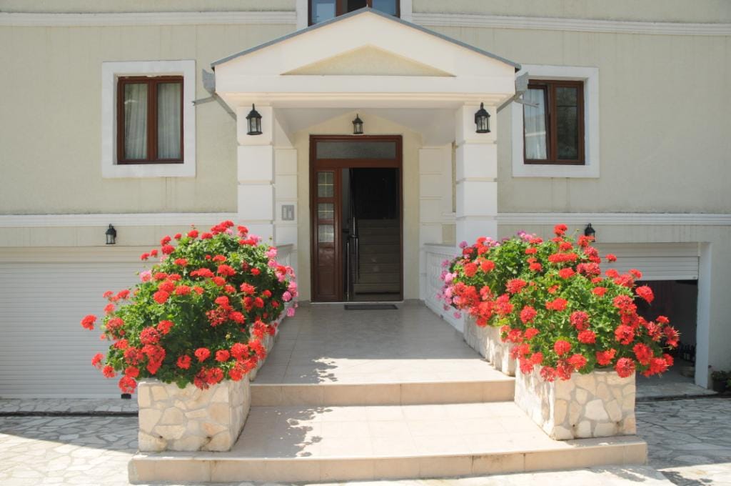 Entrance to a villa in Markovichi, Montenegro: a porch with red flowers, stone cladding, and garage doors on the facade.