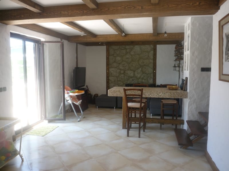 Living room with a stone wall and wooden beams in a villa in Bigovo, Montenegro: dining area and access to the terrace.