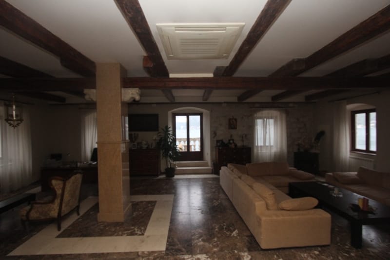 Spacious villa living room in Prčanj, Montenegro: marble floor, wooden ceiling beams, and sea view.