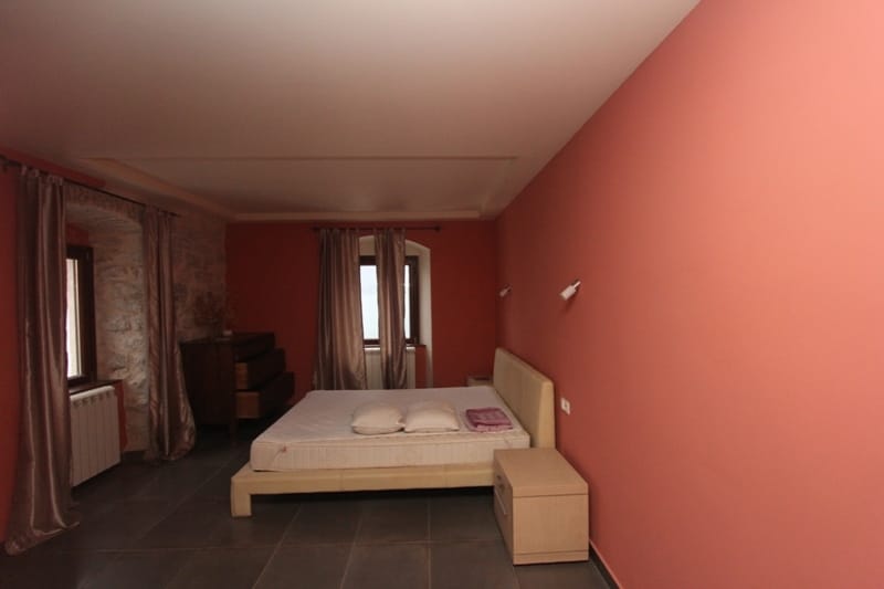 Bedroom in a villa in Prčanj, Montenegro: double bed, stone walls, tiled floor, and sea view.
