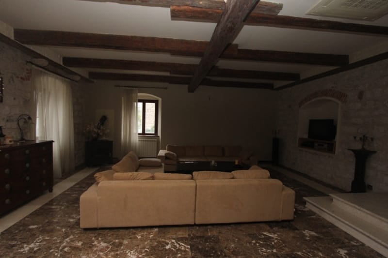 Villa living room in Prčanj, Montenegro: stone walls, wooden ceiling beams, marble floor, and soft seating.