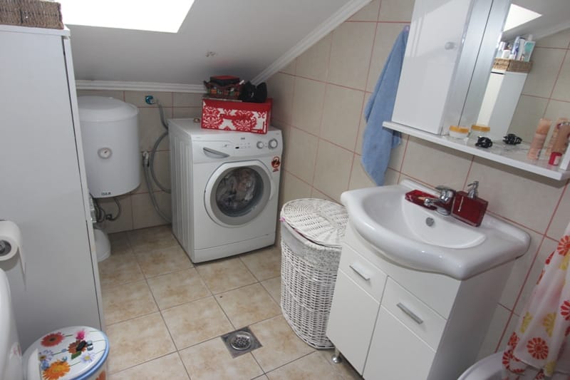Bathroom in the attic of a house in Muo, Montenegro: washing machine, water heater, sink with vanity, and tiled finish.