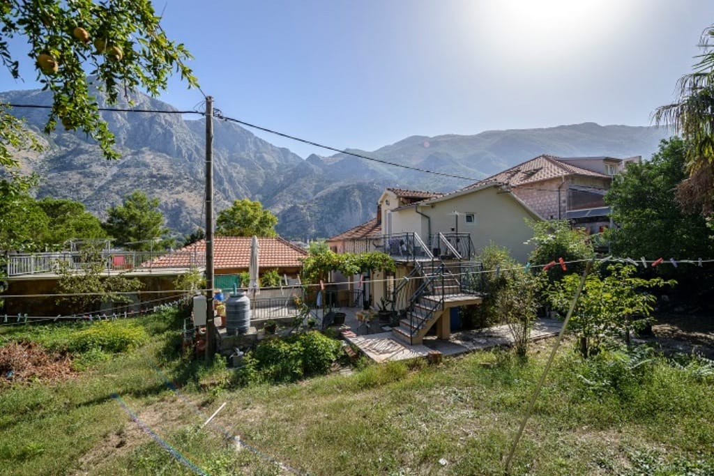 Two-story house in Muo, Montenegro, with a terrace, garden, and scenic mountain views on a sunny day.