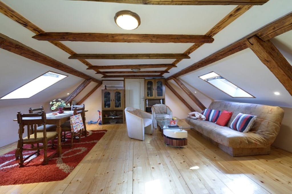 Living room in the attic of a house in Muo, Montenegro: wooden beams, dining area, soft seating, and skylight windows.