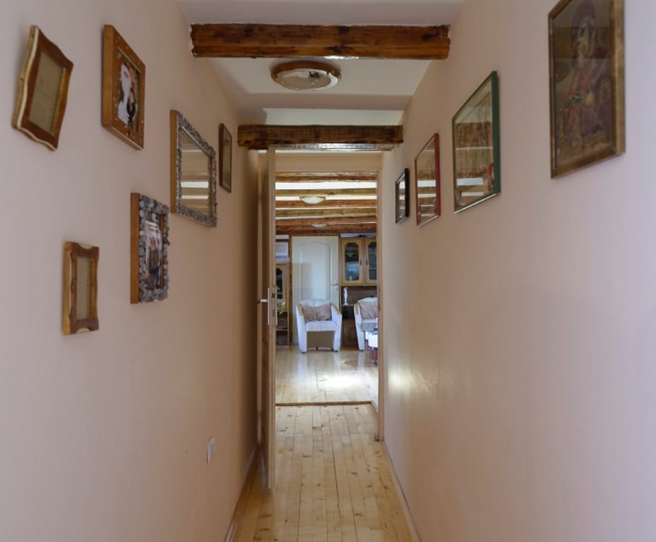 Hallway with wooden beams and paintings in a house in Muo, Montenegro, leading to a bright living room with parquet flooring.