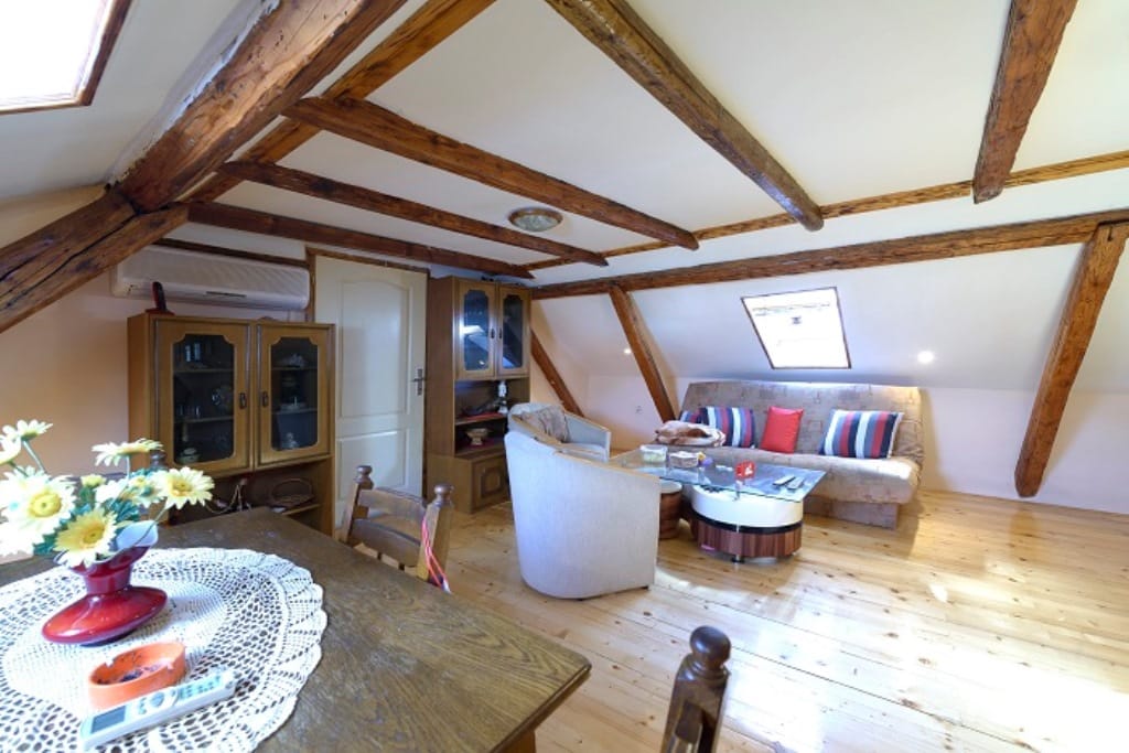 Living room in the attic of a house in Muo, Montenegro: wooden beams, parquet flooring, soft seating, and a dining area.