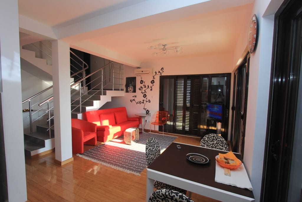Living room with a red sofa and staircase in an apartment in Rafailovići, Montenegro: modern interior with a dining area.