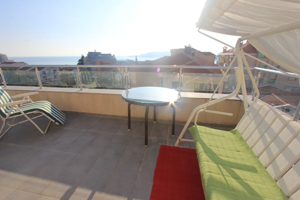 Spacious balcony with furniture and sea view in an apartment in Rafailovici, Montenegro: swing, table, and sun lounger.