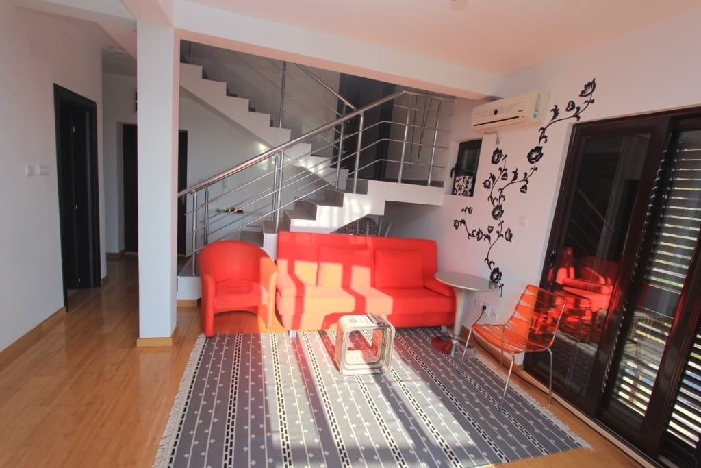 Living room in an apartment in Rafailovici, Montenegro: red furniture, staircase with railing, and panoramic glazing.