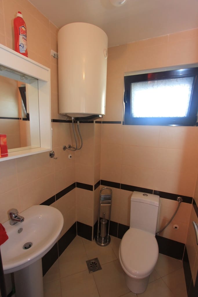 Bathroom in an apartment, Rafailovici, Montenegro: beige tiles, water heater, sink, toilet, and window.