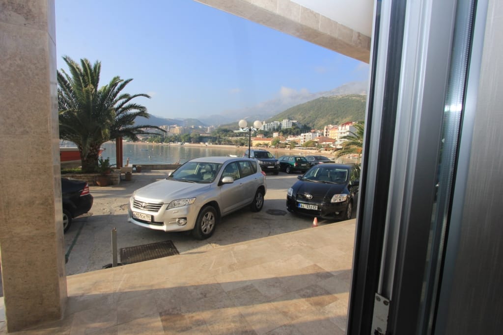 View from the terrace of a commercial property in Rafailovići, Montenegro: seaside parking, palm trees, and mountain scenery.
