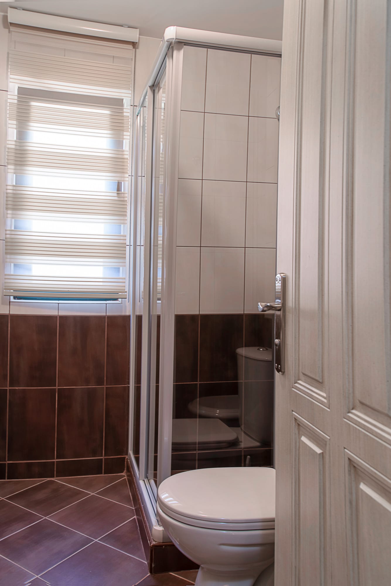 Bathroom in a townhouse in Lastva, Montenegro: shower cabin, light-colored tiles, and a window with blinds.