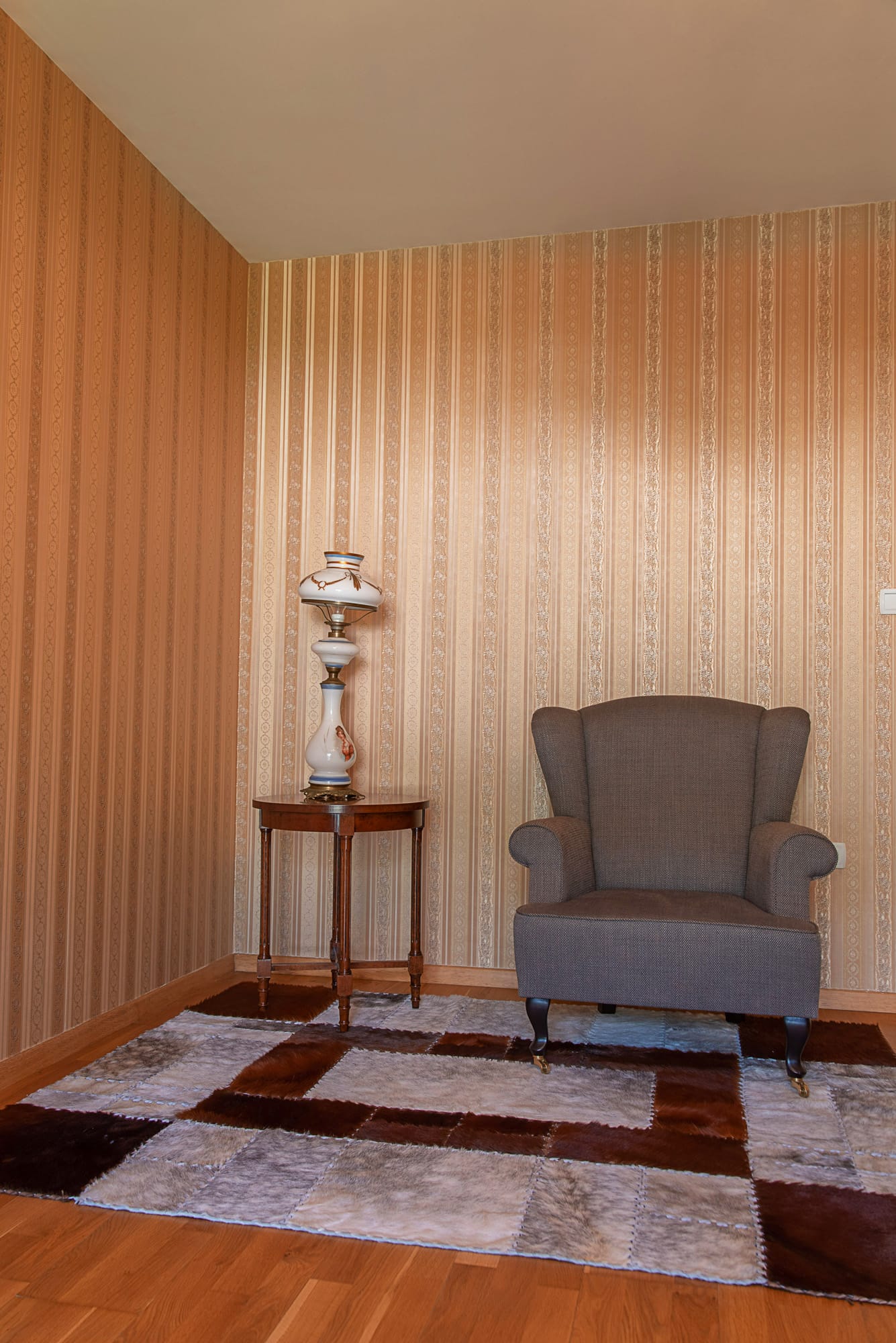 A cozy relaxation corner in the townhouse living room in Lastva, Montenegro: an armchair, a vintage lamp, and a fur rug.