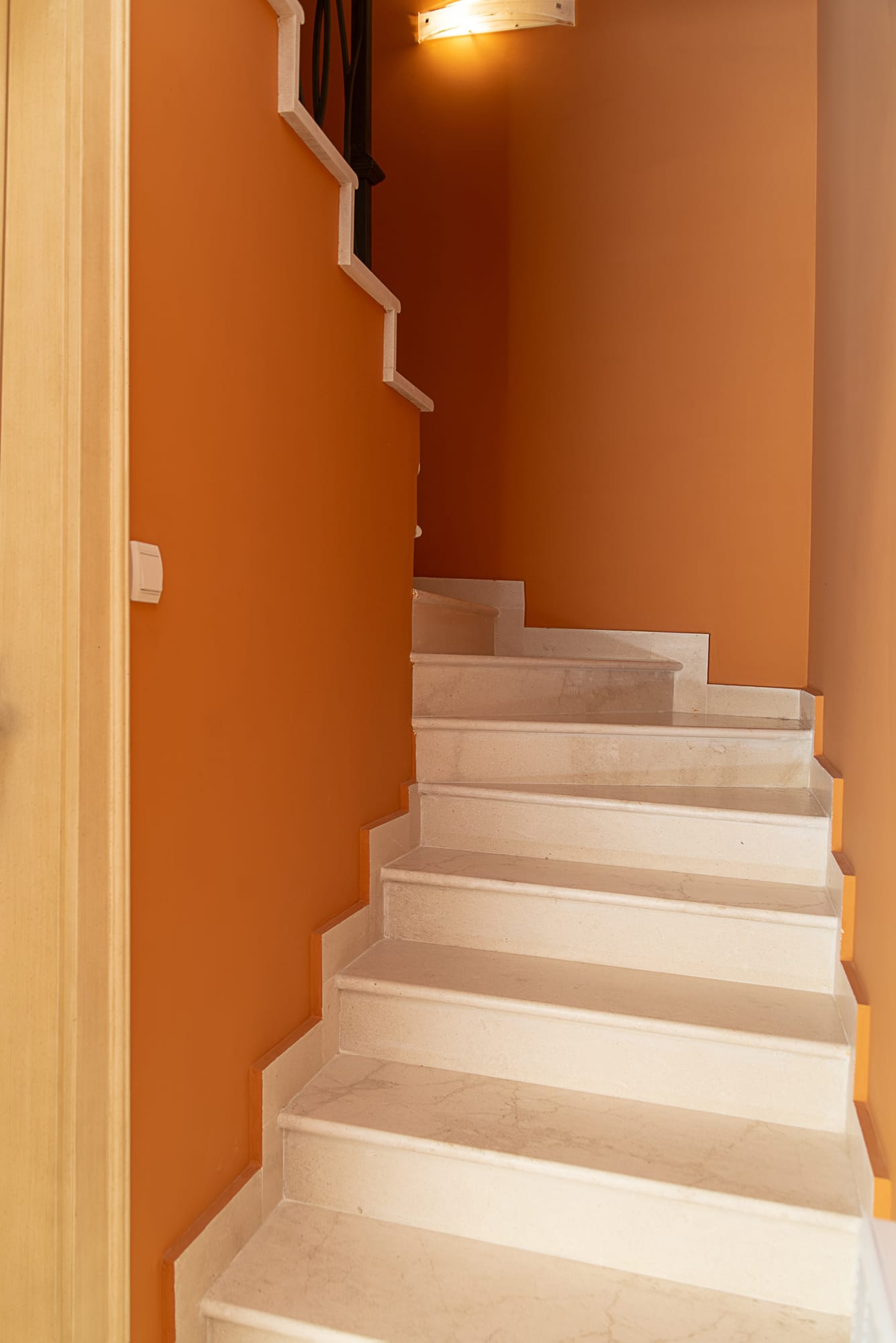 Marble staircase in the interior of a townhouse in Lastva, Montenegro, with bright orange walls and wrought-iron railings.
