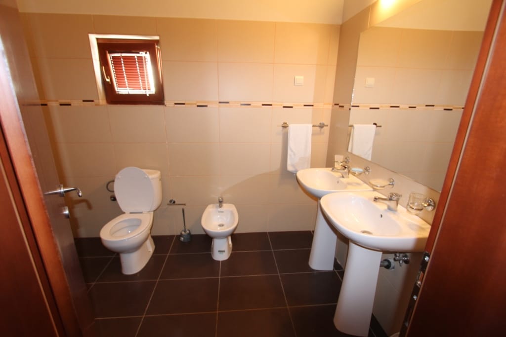 Bathroom in a mini-hotel in Igalo, Montenegro: two sinks, toilet, bidet, beige tiles, and dark flooring.