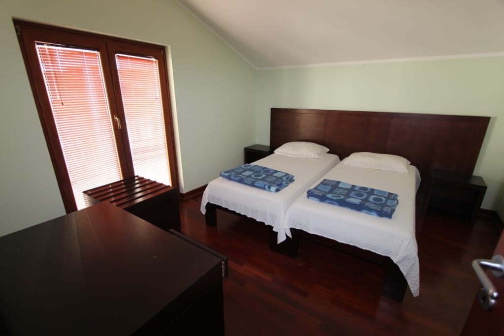 Bedroom with two beds, dark furniture, and parquet flooring in a mini-hotel in Igalo, Montenegro. View of the balcony with blinds.