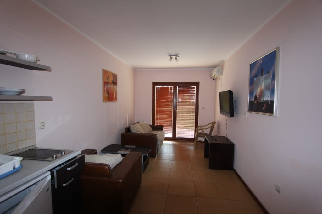 Living room with kitchen in the Igalo mini-hotel, Montenegro: leather sofas, TV, stove, and access to a terrace with blinds.