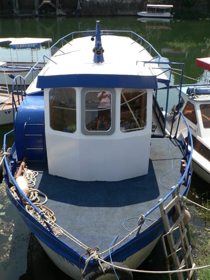 A pleasure boat at the restaurant pier in Virpazar, Montenegro: view of the deck with blue covering and the vessel’s wheelhouse.