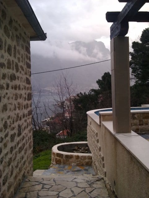 Sea and mountain view from the terrace of a stone house in Prčanj, Montenegro, with a pool and a paved path.