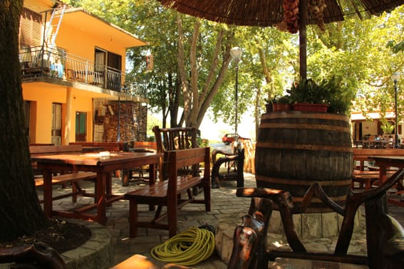 Cozy summer terrace of a restaurant in Virpazar, Montenegro: wooden furniture, wine barrel decor, and a shady garden.