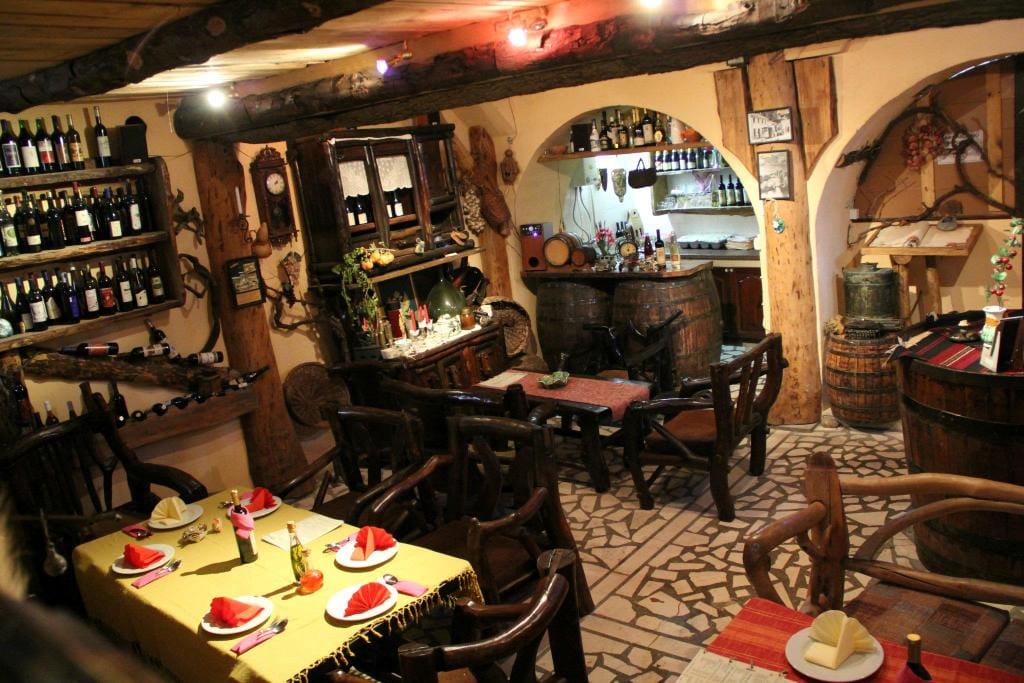 Interior of a traditional wine cellar restaurant in Virpazar, Montenegro: wooden furniture, wine barrels, and shelving.