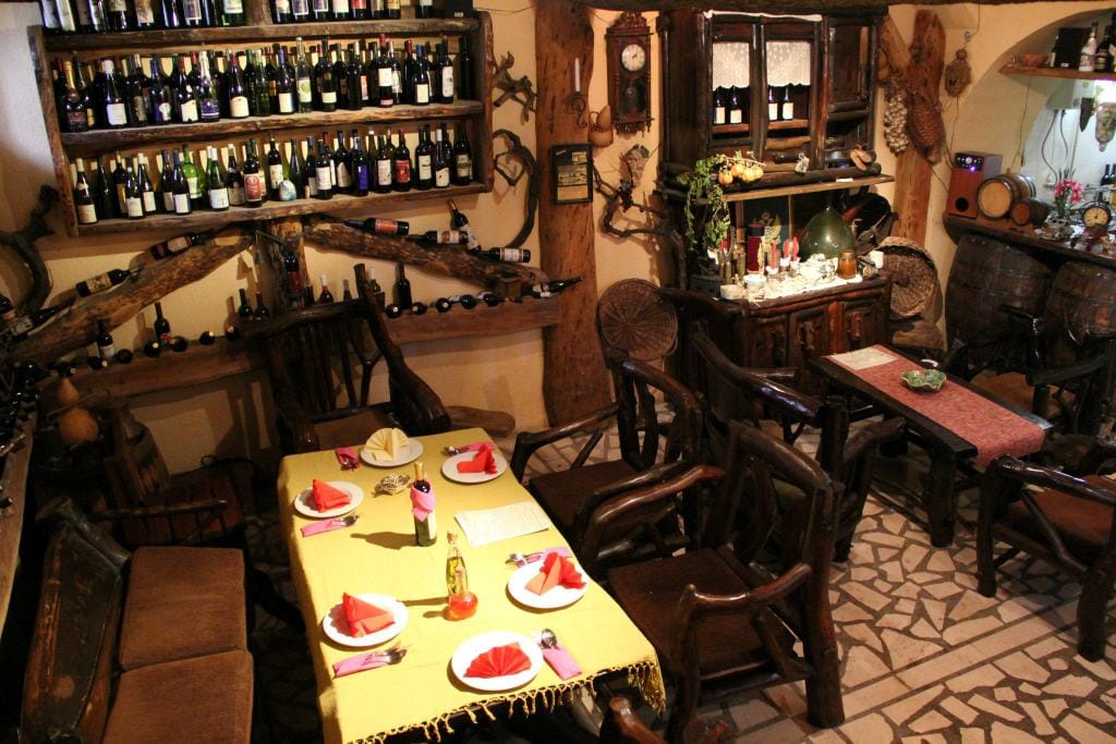Interior of a traditional wine restaurant in Virpazar, Montenegro: wooden furniture, wine shelves, and a stone floor.