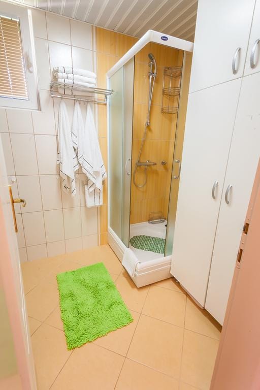 Bathroom with a shower cabin and a white cabinet in a house, Krimovica, Montenegro. Light tiles and a bright green rug.