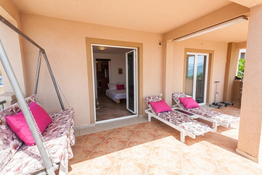 Spacious terrace with loungers and a swing in a house in Krimovica, Montenegro, view of the bedroom with tiled floor.