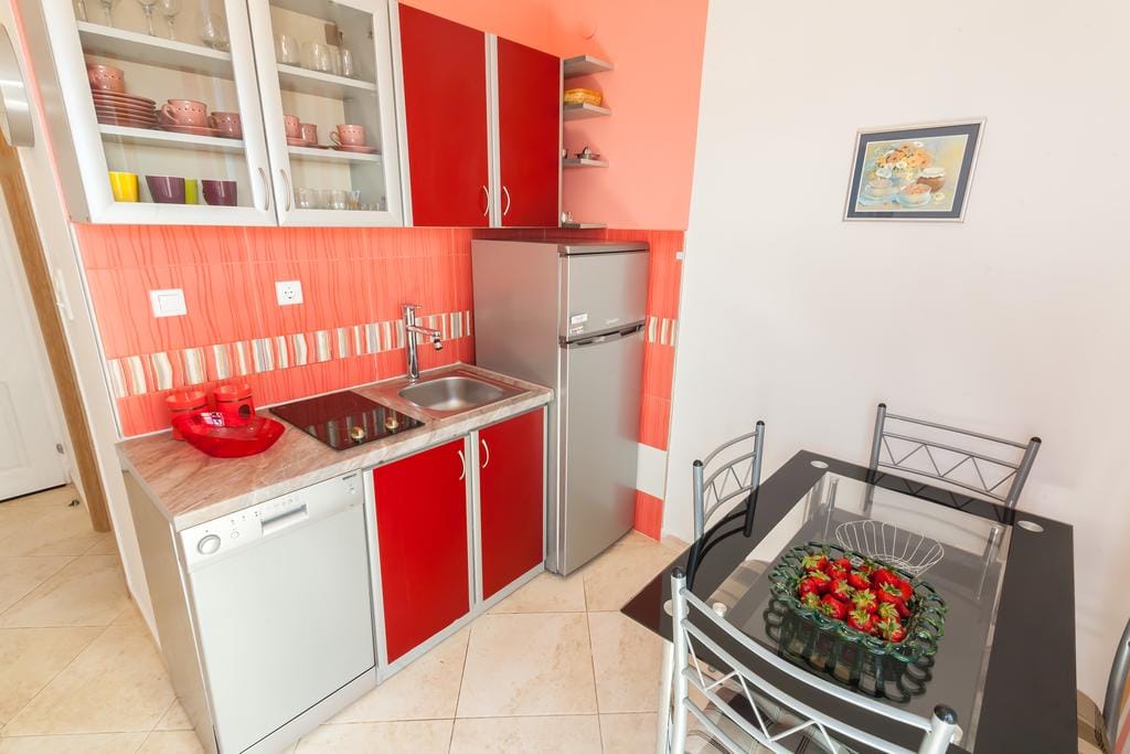 Bright kitchen with red cabinets, appliances, and a dining table in a house for sale in Krimovica, Montenegro.