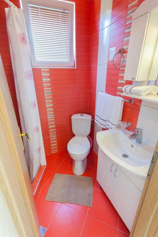 Bathroom with red tiles, shower, and white fixtures in a house for sale, Krimovica, Montenegro.