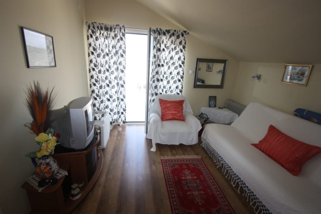 Cozy living room in a house in Uteha, Montenegro: light furniture, a rug, TV, and access to a balcony with sea view.