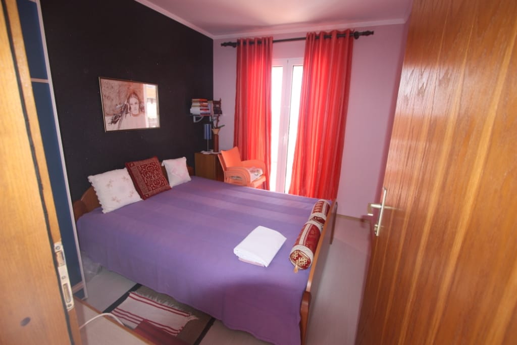 Bedroom with a double bed and red curtains in a house for sale, Utjeha, Montenegro. Interior with a dark wall.