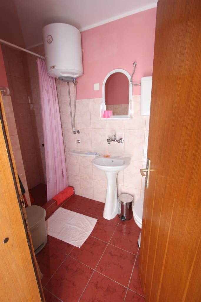 Bathroom in a house in Utjeha, Montenegro: shower with a pink curtain, sink, water heater, and tiled finish.