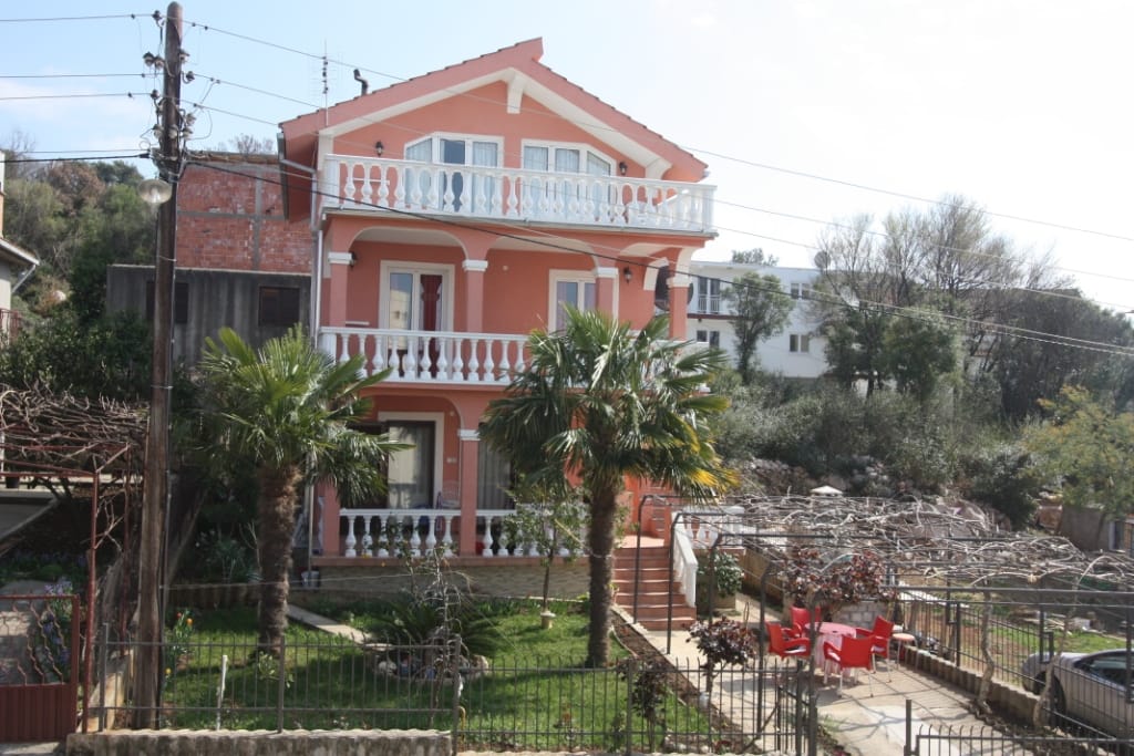 Three-story pink house with white balustrades and palm trees in the yard, Utjeha, Montenegro.