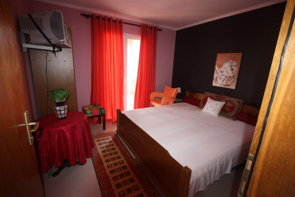 Bedroom in a house in Utjeha, Montenegro: double bed, red curtains, dark accent wall, and access to the balcony.