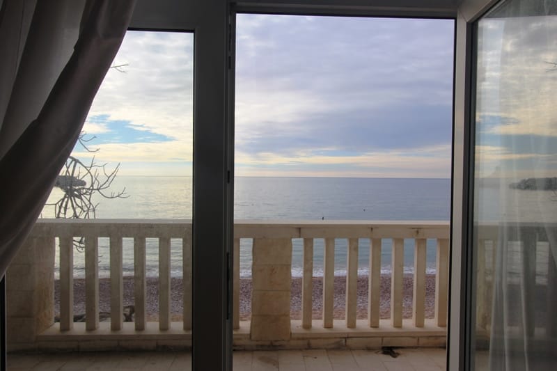 Sea and beach view from the apartment balcony in Sveti Stefan, Montenegro: stone railings and panoramic windows.